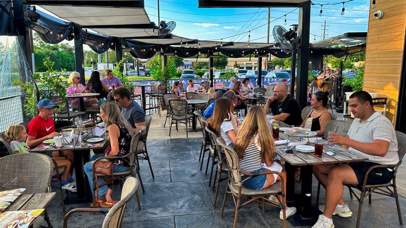 Patrons enjoy dining on a spacious outdoor patio with a live musician playing guitar.