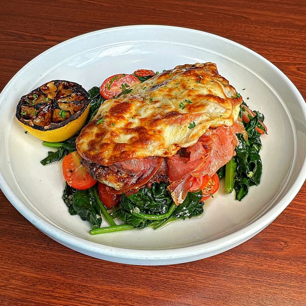 Baked chicken topped with melted cheese and prosciutto, served with spinach, tomatoes, and grilled lemon.