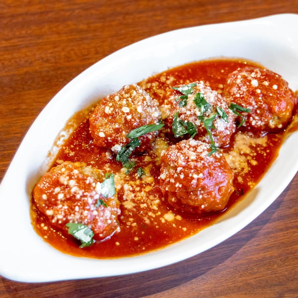Meatballs in red sauce, topped with grated cheese and fresh herbs, in a white dish.