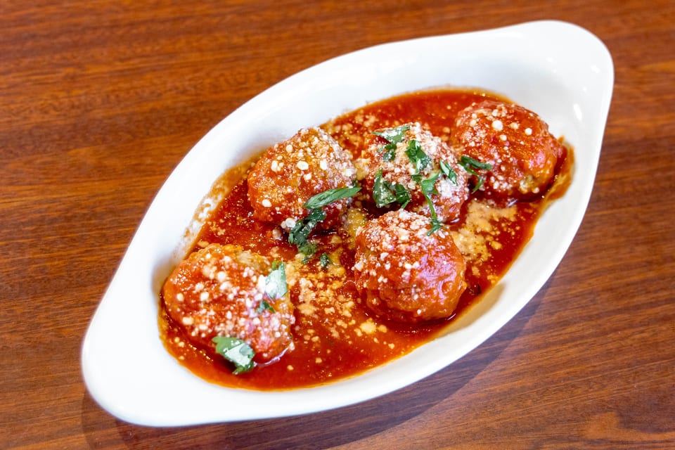 Meatballs in red sauce, topped with grated cheese and fresh herbs, in a white dish.